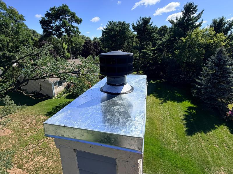 A new galvanized chase cover with a round cap under a blue sky
