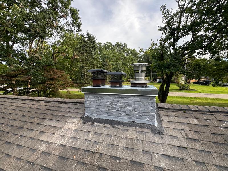 A grey painted masonry chimney with a new cover and a stainless cap