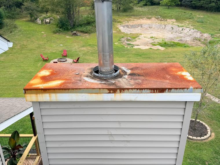 A rusted chase cover staining the siding below it